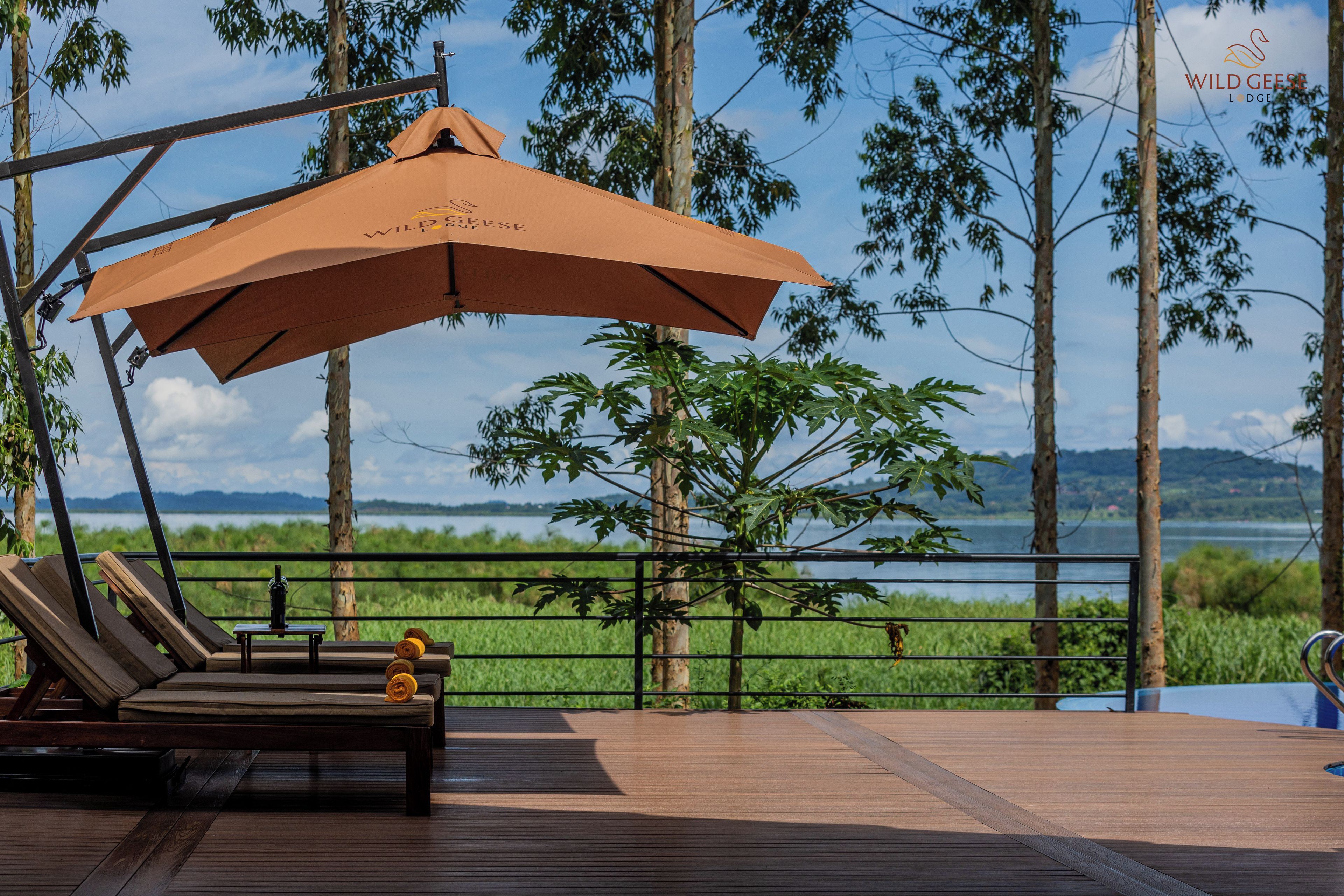 A wooden deck with lounge chairs and an umbrella, overlooking a body of water and greenery.