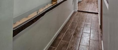 Un pasillo con piso de madera, pared blanca y una ventana al final.