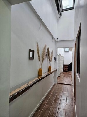 A hallway with a wooden floor, a white wall, and a window at the end.