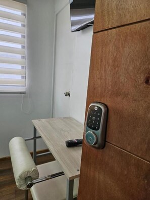 A room with a wooden wardrobe, a small table, a remote control, and a white towel on a chair.