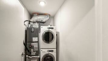 A laundry room with two stacked washing machines and a dryer, a vent above the machines, and a door on the left.