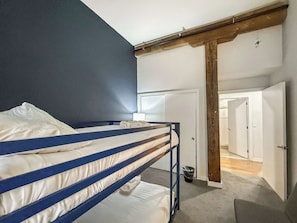A bunk bed with white bedding, a wooden ceiling beam, and a white door leading to another room. - Luxury 2BD | 4 Beds | Northern Liberties (Philadelphia)