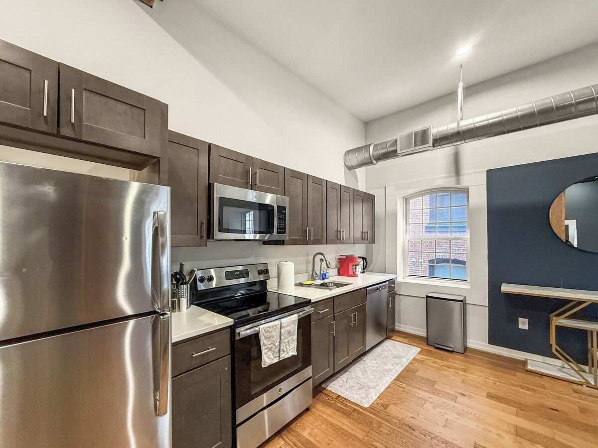 A modern kitchen with stainless steel appliances, dark cabinetry, and a window providing natural light.