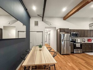 A modern kitchen with stainless steel appliances, a wooden dining table, and a view into the adjacent living area. - Luxury 2BD | 4 Beds | Northern Liberties (Philadelphia)