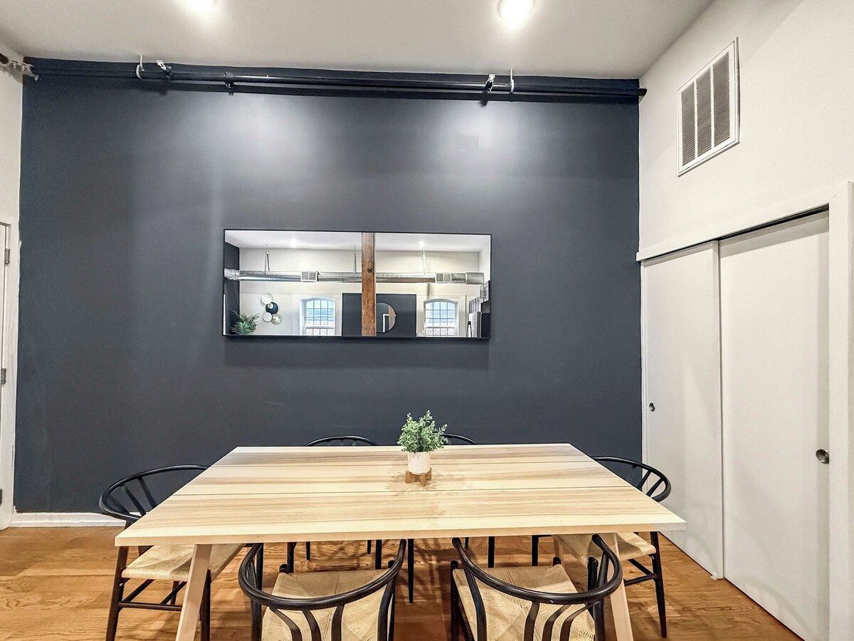 A dining area with a long wooden table, black chairs, and a small plant centerpiece.