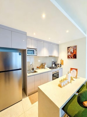 A modern kitchen with stainless steel appliances, a central island, and a painting on the wall. - Luxury GTC Westlands Suite | Pool, Gym, Cinema, Sauna, Skyline Views & Mall (Nairobi)