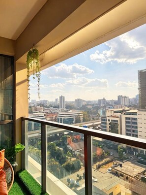 A balcony with a city view, a hanging plant, and a cushioned chair. - Luxury GTC Westlands Suite | Pool, Gym, Cinema, Sauna, Skyline Views & Mall (Nairobi)