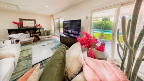 A modern living room with a flat-screen TV, comfortable seating, a coffee table, and a view of a pool and greenery. - 1 Mi to Old Town | Saltwater Pool + Spa | EV Charger (Scottsdale)