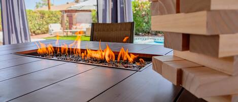 A fire feature with a clear view of a pool and greenery in the background.