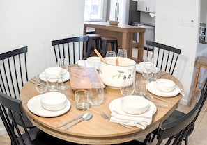 A dining table set for four with plates, glasses, and cutlery, surrounded by black chairs in a room with a kitchen in the background. - 1 Mi to Old Town | Saltwater Pool + Spa | EV Charger (Scottsdale)