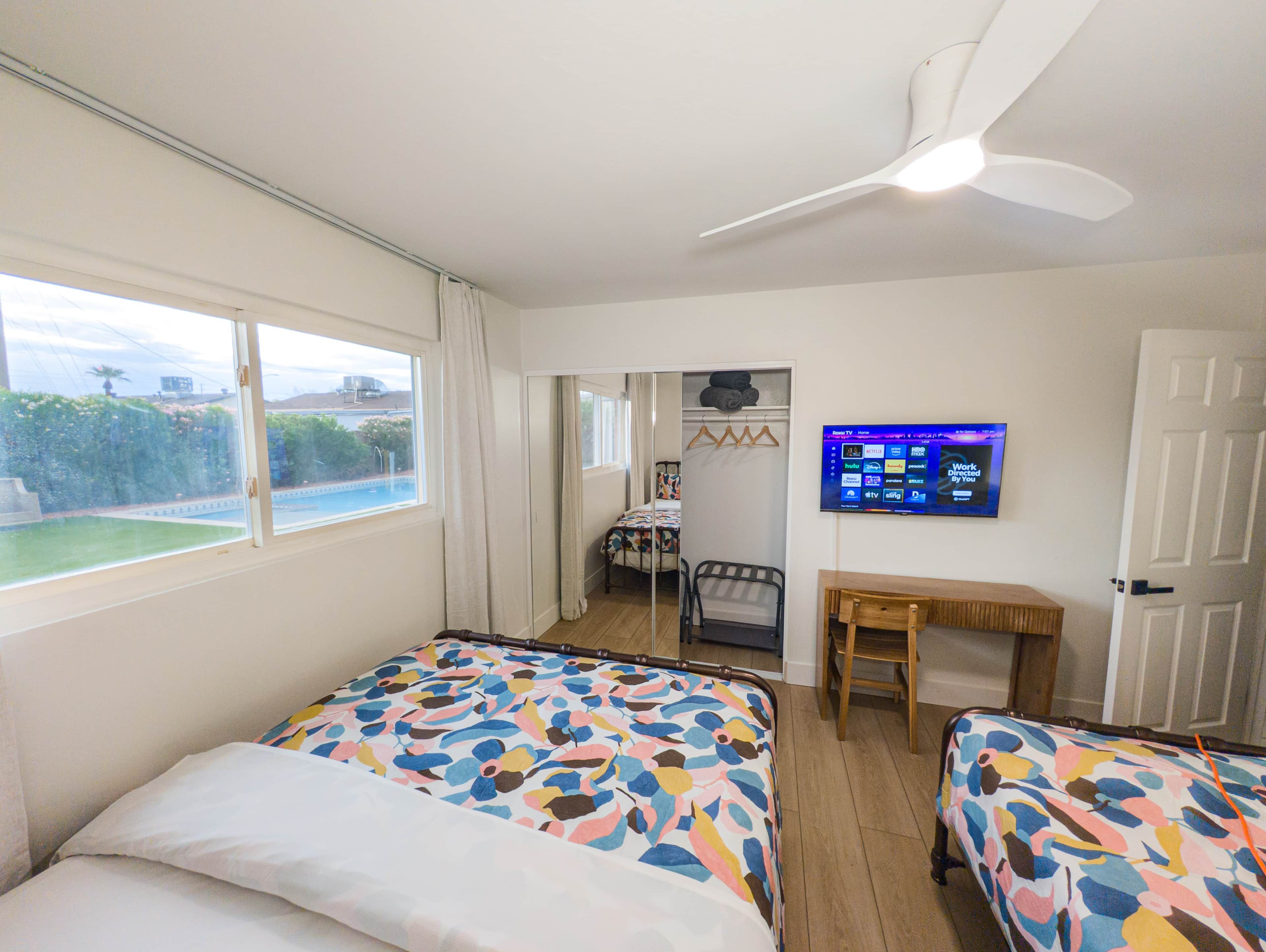 Habitació d'hotel amb dos llits, un escriptori, una televisió i vista a una piscina.