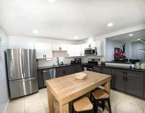 A modern kitchen with stainless steel appliances, white cabinetry, and a wooden dining table with stools. - 1 Mi to Old Town | Saltwater Pool + Spa | EV Charger (Scottsdale)