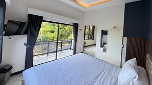 A hotel room with a large bed, a television, a balcony with a view, and a door with a mirror. - Hostel Labuan ORA (Labuan bajo)