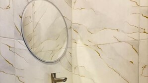 A bathroom with a white sink, a round mirror, and a marble-patterned wall. - Hostel Labuan ORA (Labuan bajo)