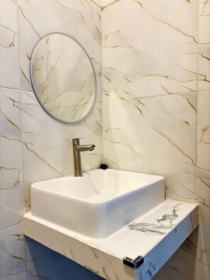 Une salle de bain avec un lavabo blanc, un miroir rond et un mur décoré d’un motif marbré.