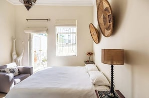 A bedroom with a bed, a nightstand, a lamp, a chair, and a window with bars. - Selah - Victorian Villa in Vredehoek (Cape Town)