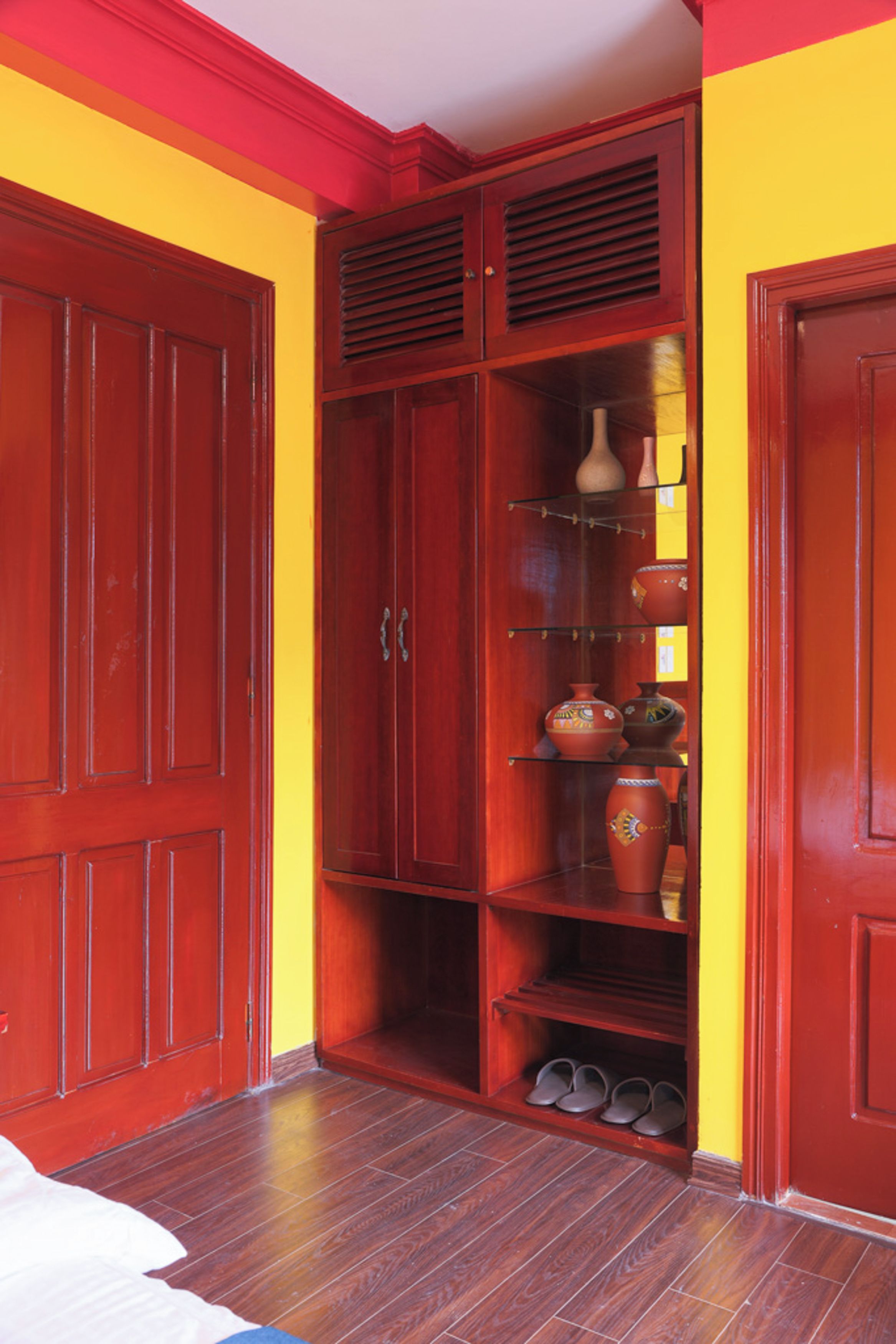A wooden wardrobe with multiple doors and shelves, a pair of shoes on the lower shelf, and a vase on the top shelf.