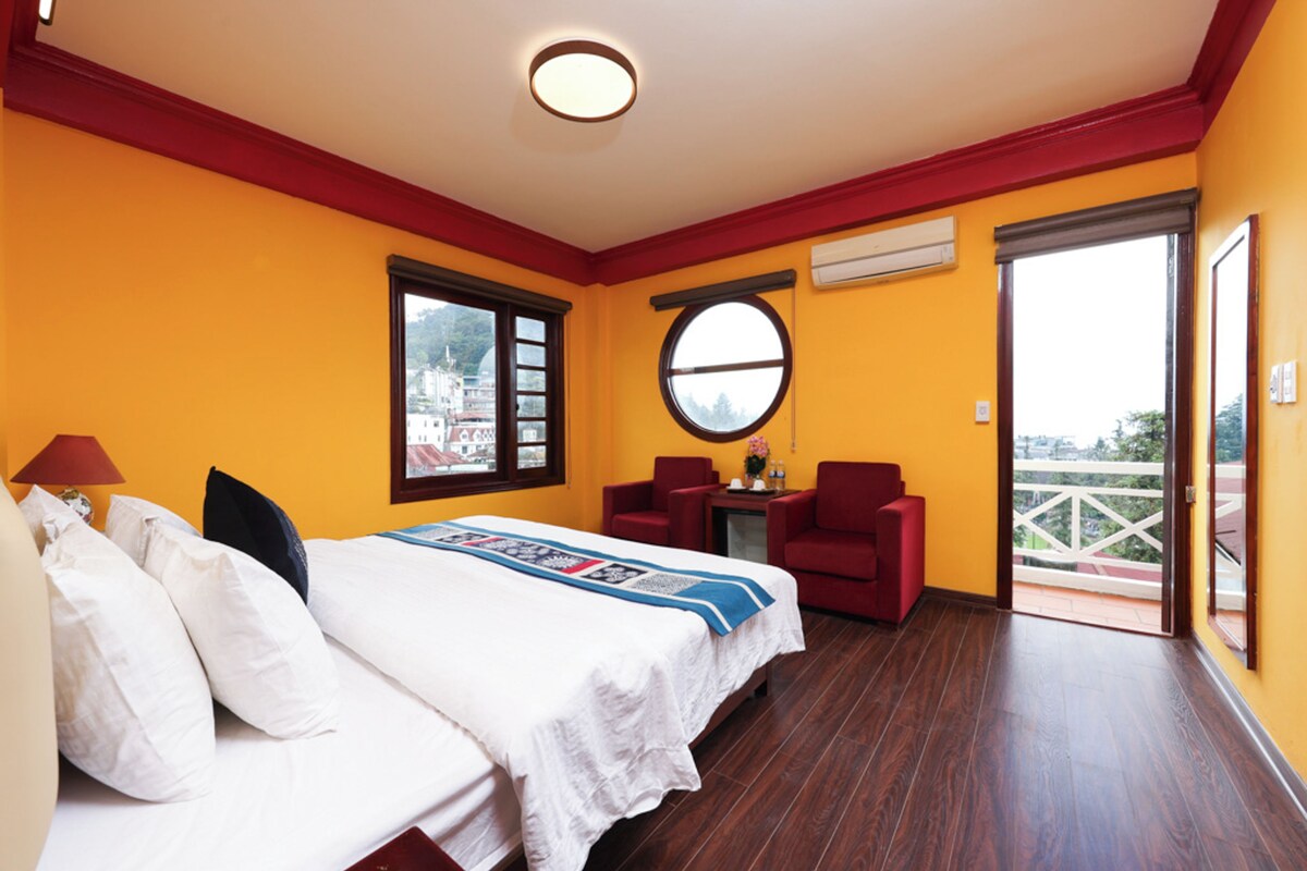 Een hotelkamer met twee bedden, een bureau, een stoel en een balkon met uitzicht.