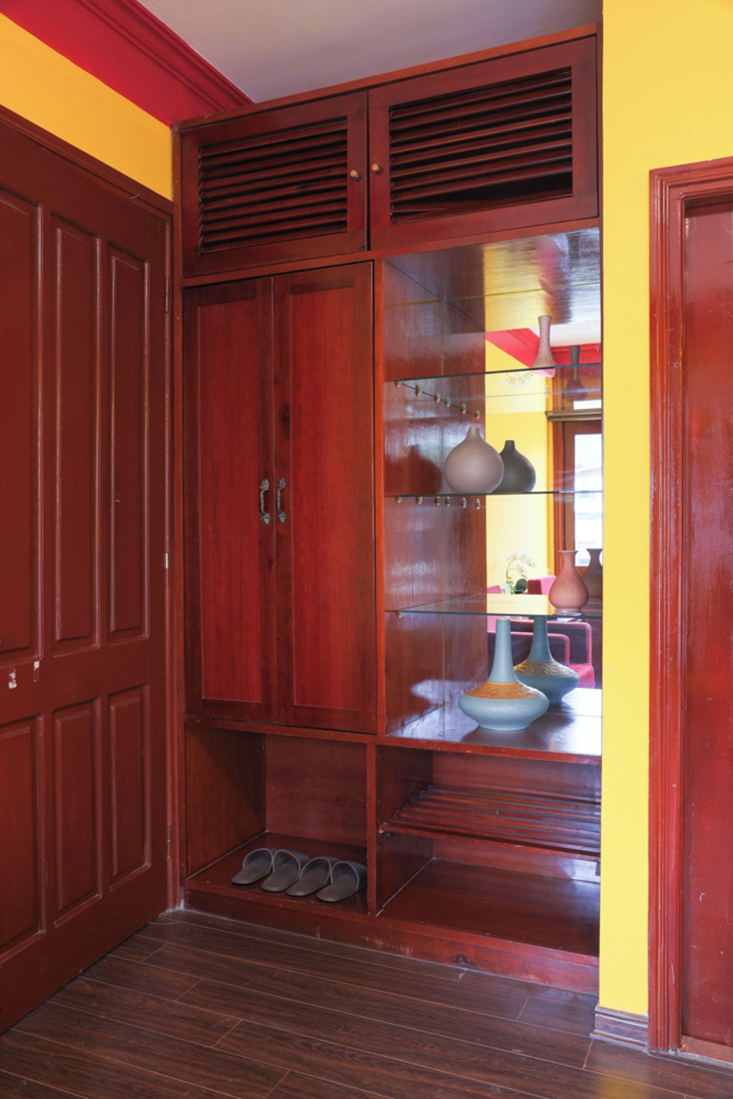 A wooden wardrobe with a glass-fronted cabinet containing decorative items.