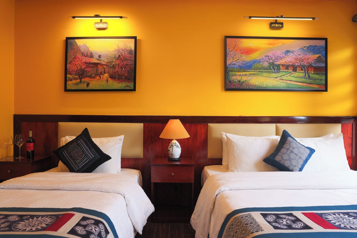 Een hotelkamer met twee bedden, een nachtkastje met een lamp en twee ingelijste schilderijen aan de muur.