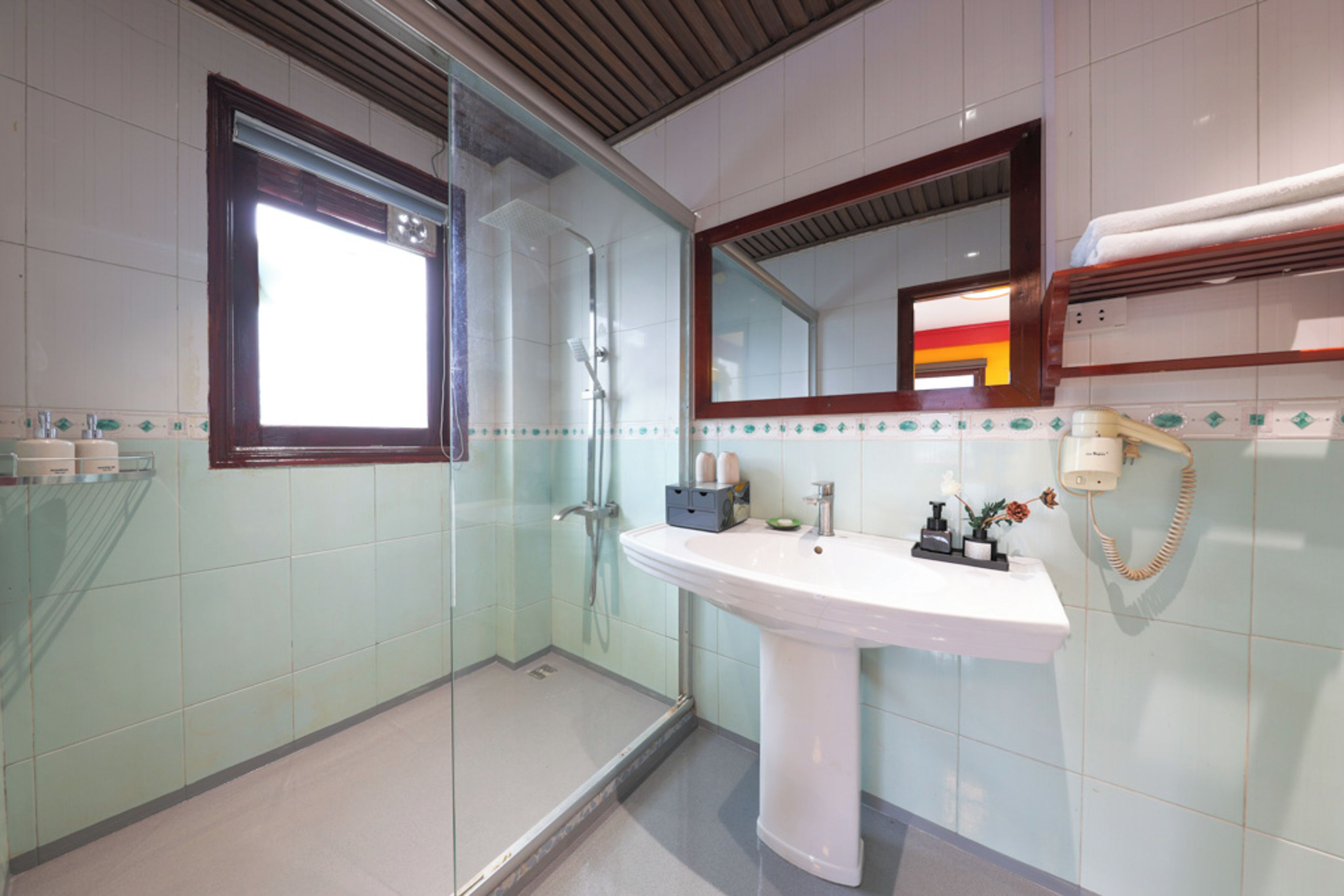 Un bany amb plat de dutxa envoltat de vidre, un lavabo blanc i un mirall a sobre.