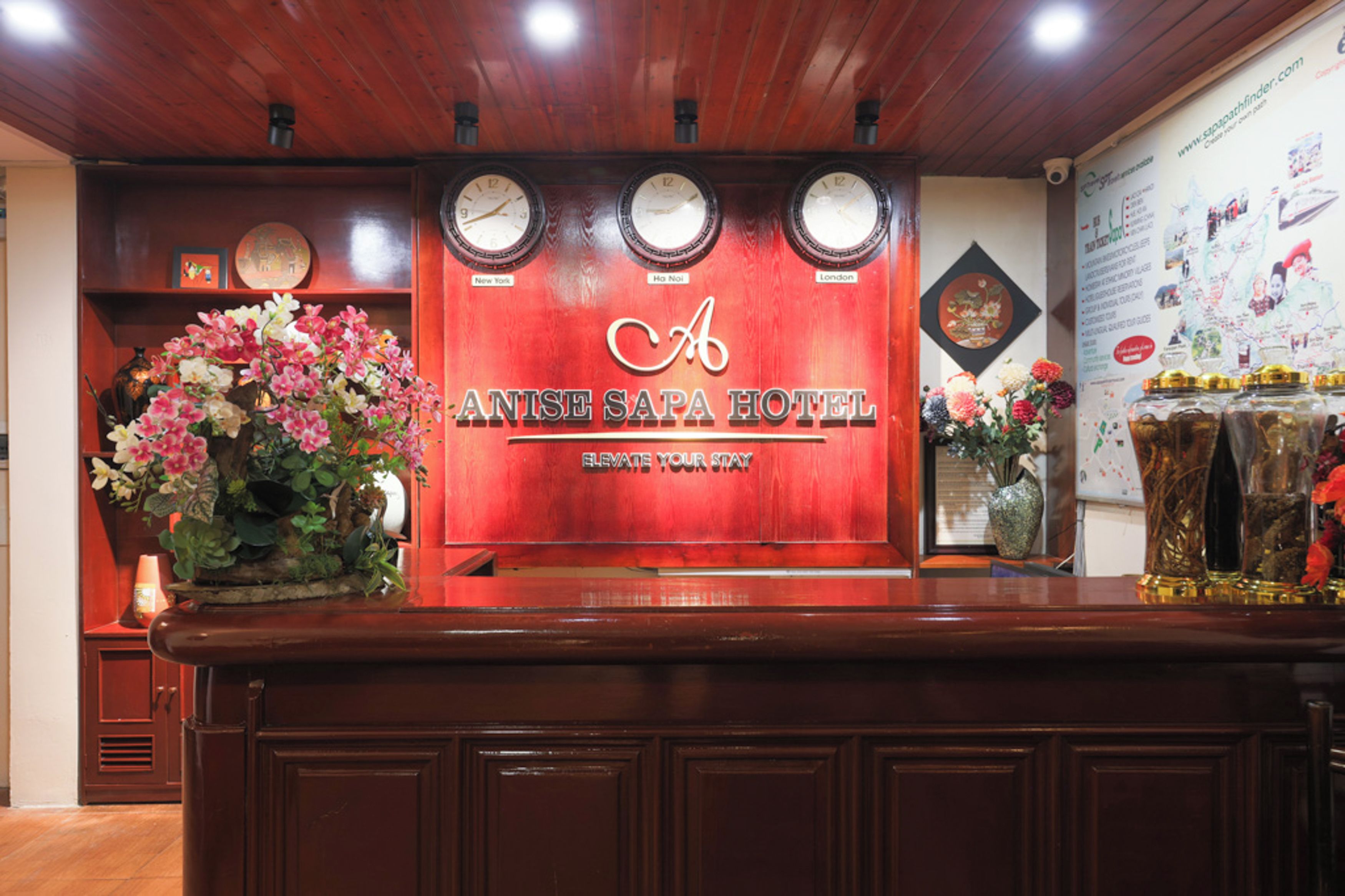 A reception desk with clocks, a floral arrangement, and a wall with a map and awards.
