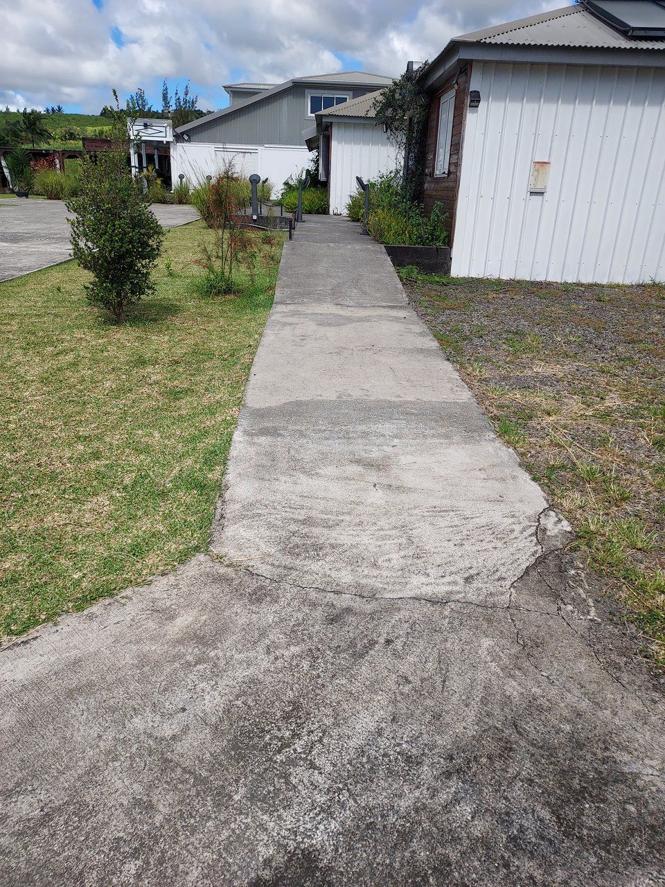 A concrete pathway leading to a row of white buildings with a grassy area on one side.