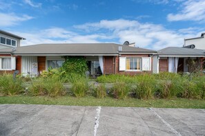 Une rangée de maisons de plain-pied, dotées d’un toit plat, d’un petit jardin devant et surplombées par un ciel dégagé.