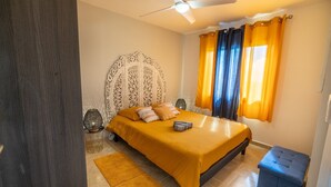 Una camera da letto con un letto, una ventola a soffitto, una finestra con tende e una lampada da comodino.