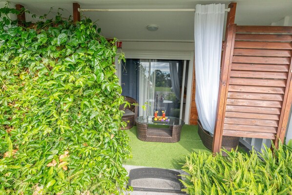 Un espacio de estar al aire libre techado con mesa de vidrio, sillas de mimbre y una pérgola de madera.