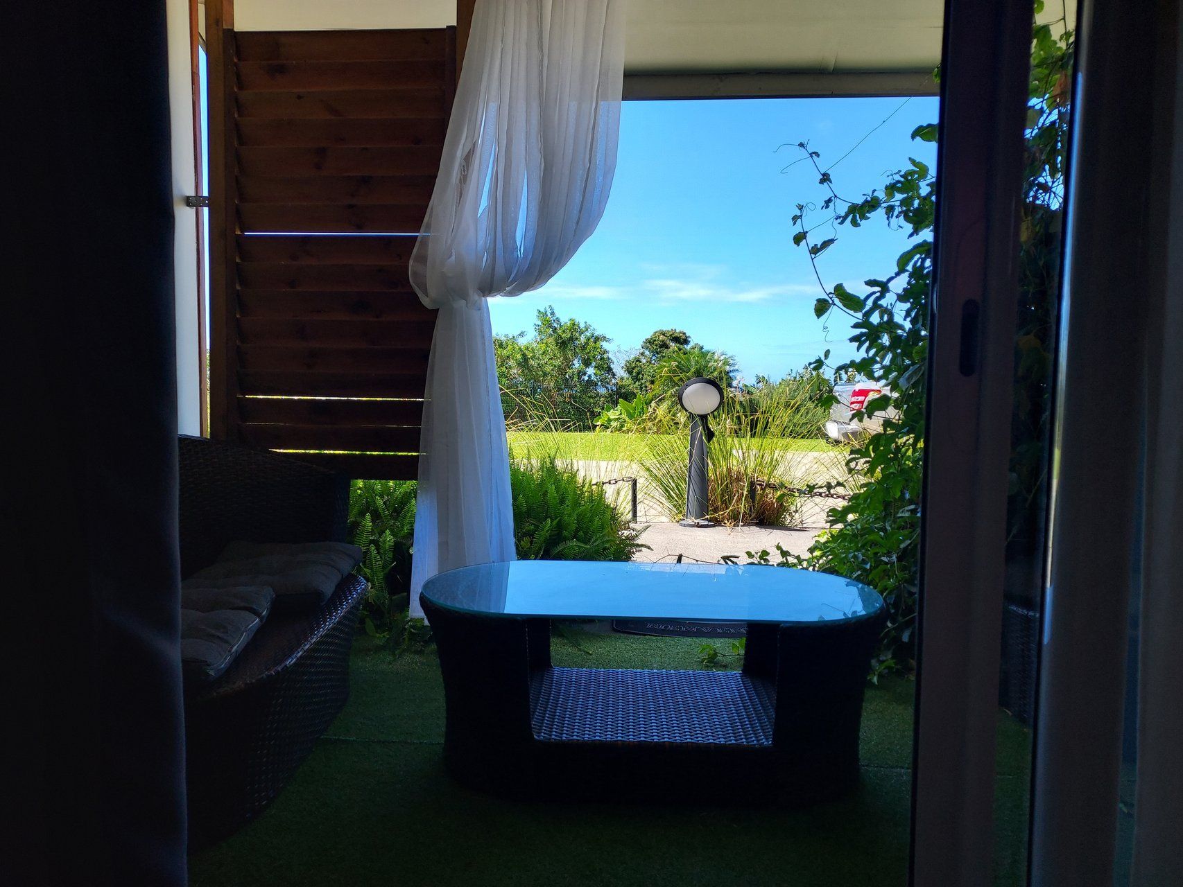 Een terras met een tafel en stoelen, een overdekte bank en uitzicht op een tuin en straat.