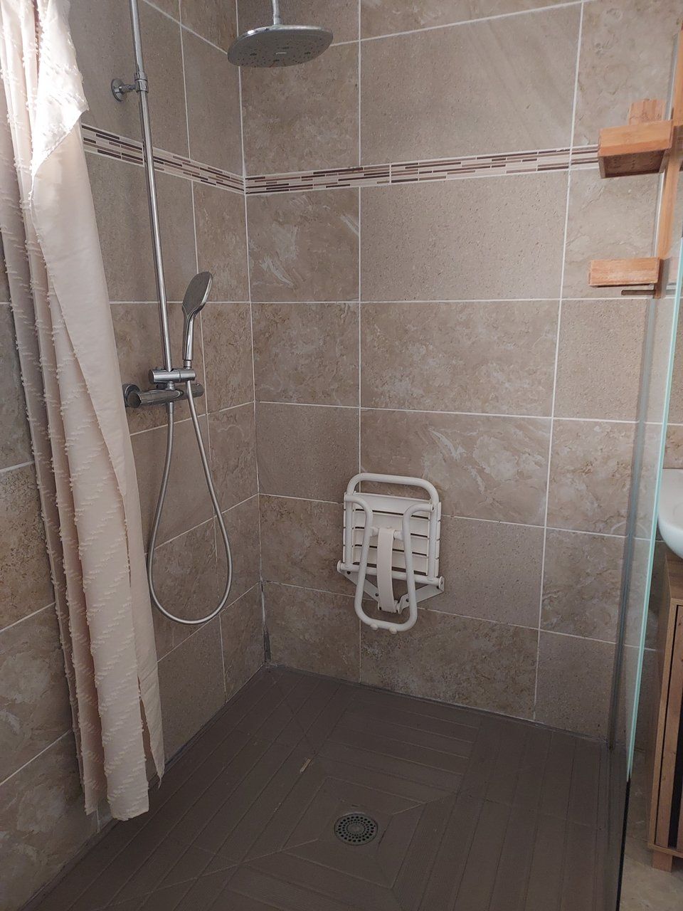Área de duche com chuveiro manual, suporte de toalha fixado na parede e painel de comando do chuveiro.