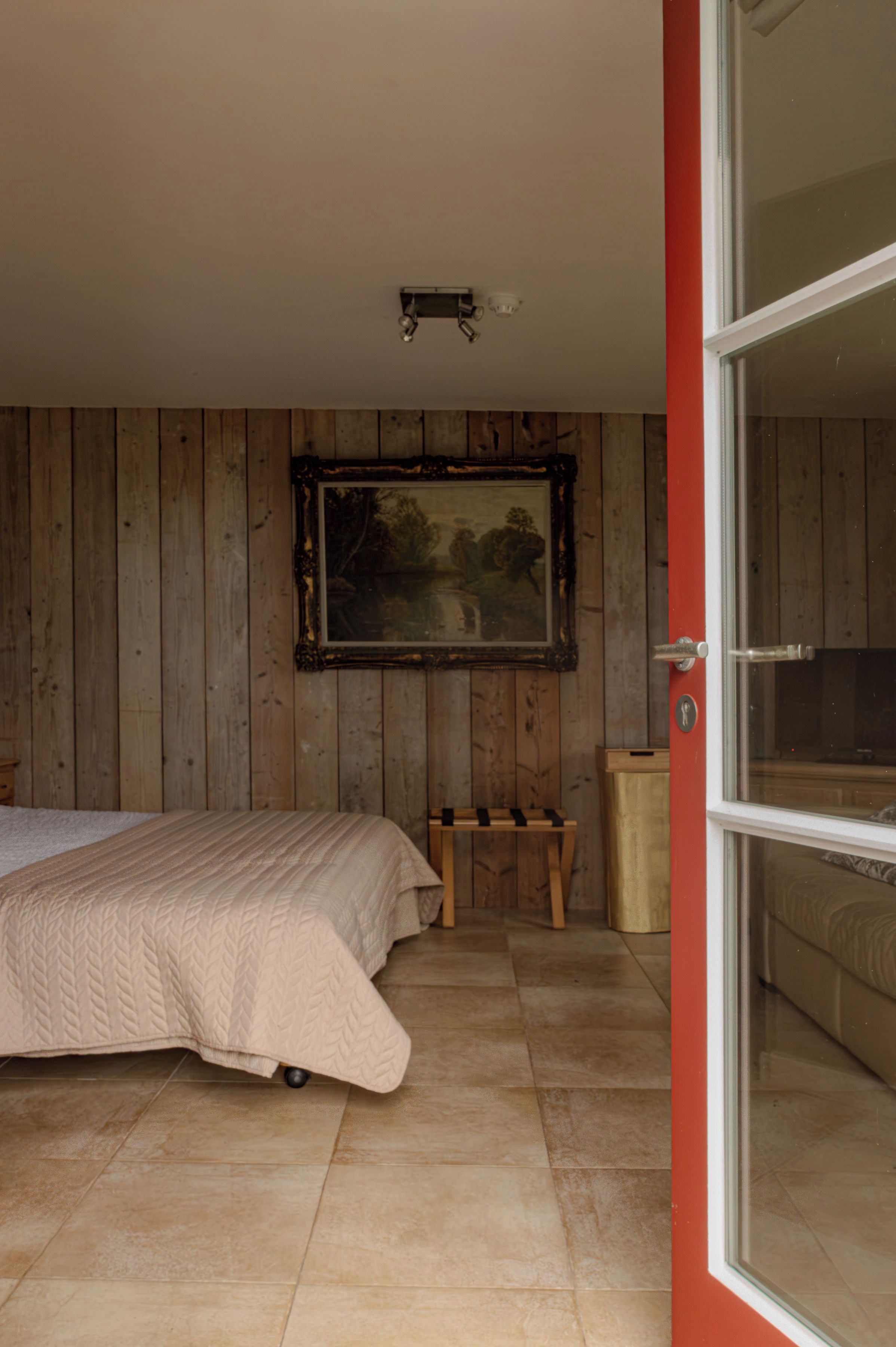 A bedroom with a bed, a wooden wall, a framed picture, and a door leading to another room.