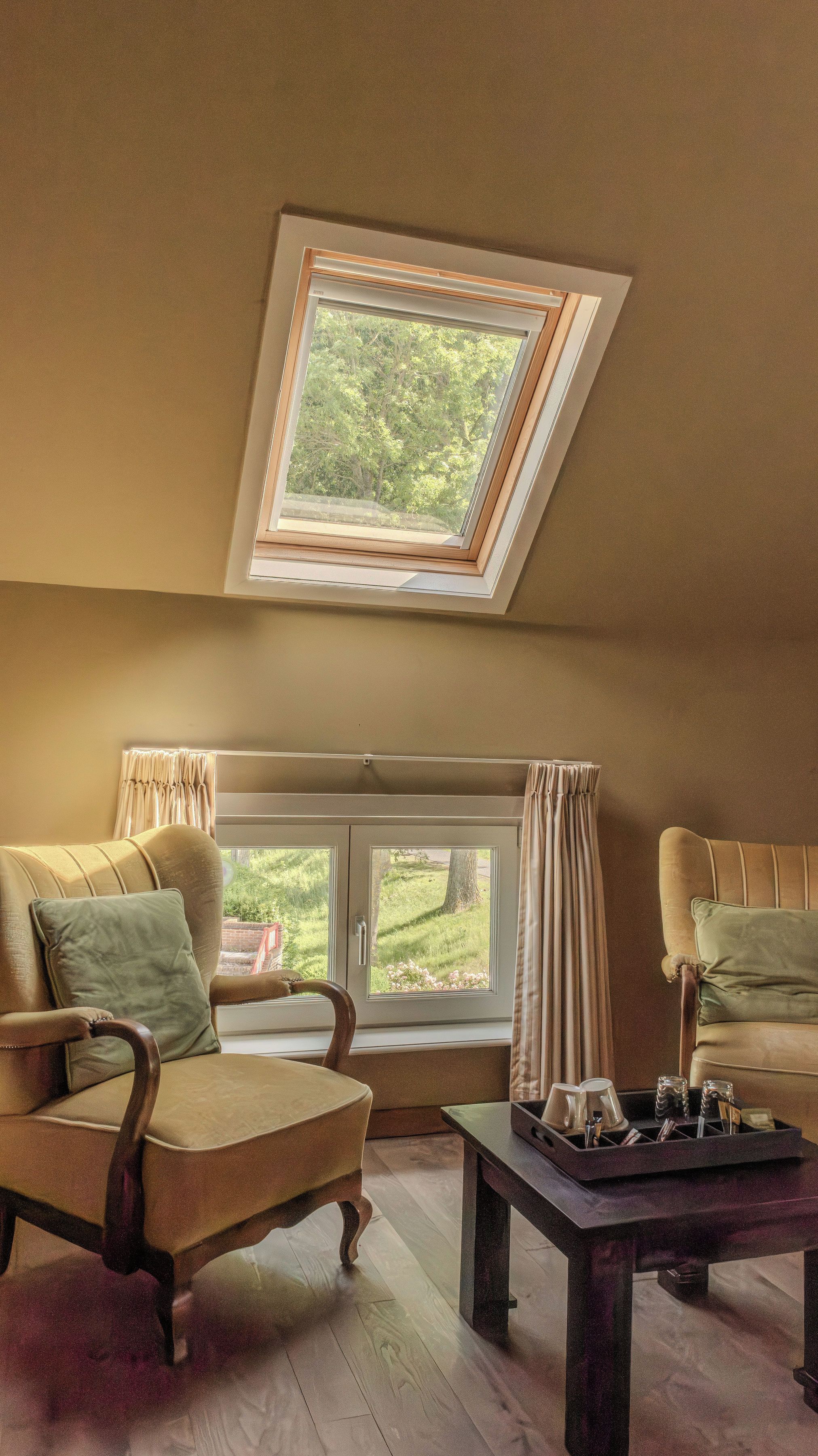 A room with a skylight, two leather armchairs, a wooden coffee table, and a view of greenery outside.