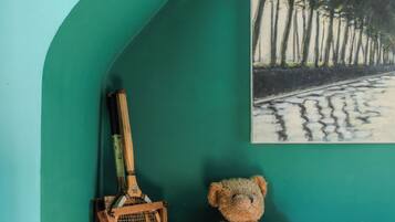 A room with a teal wall, a painting of trees, a wooden bench, and a teddy bear.