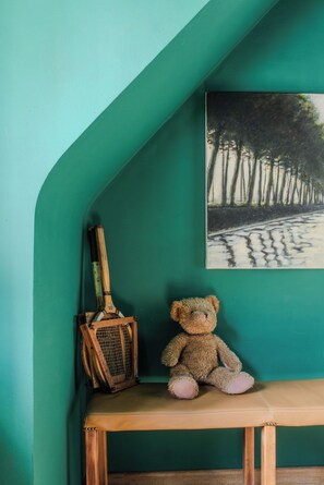 A room with a teal wall, a painting of trees, a wooden bench, and a teddy bear.