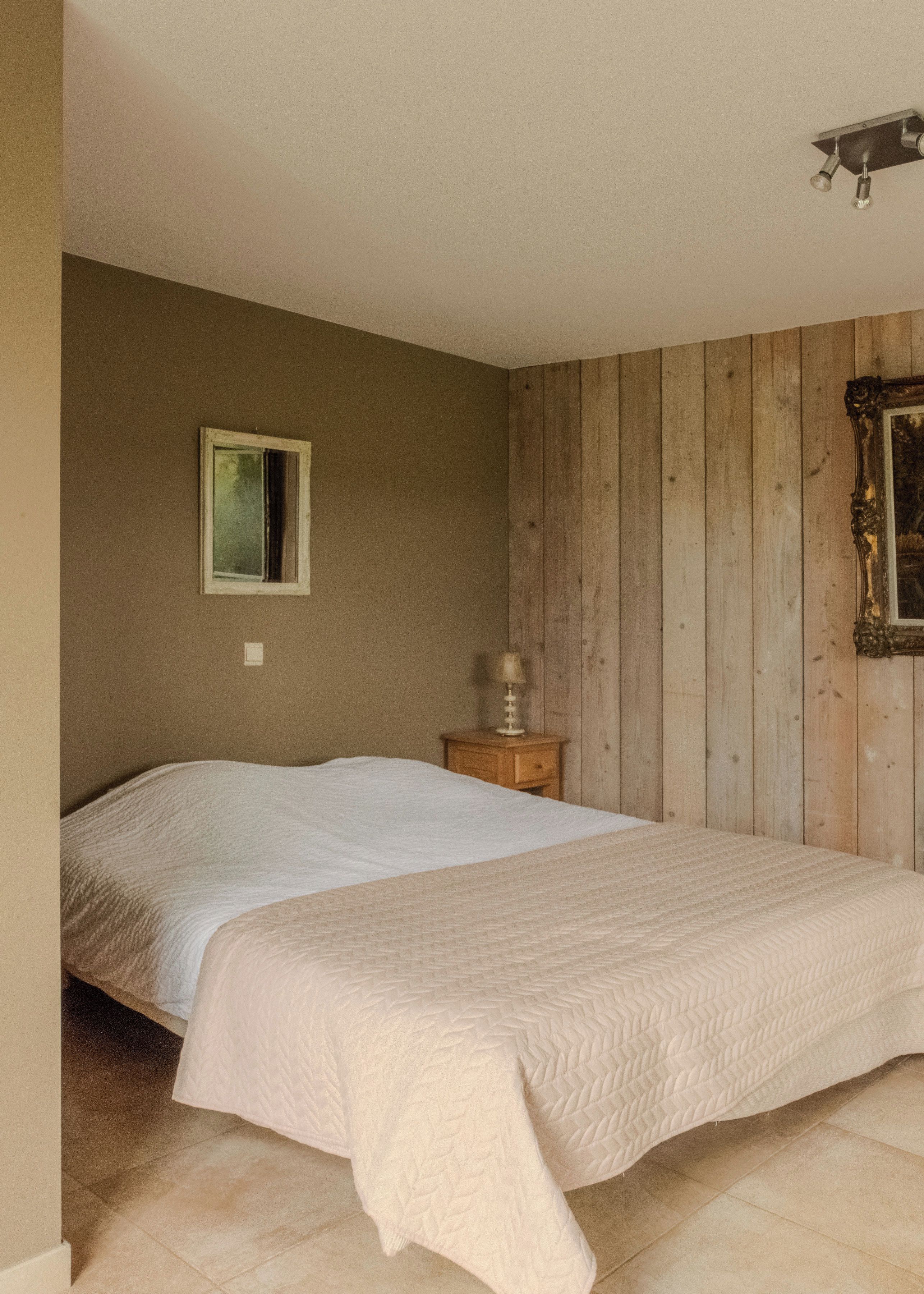 Een slaapkamer met een bed, nachtkastje, wandlamp en een houten paneelwand.