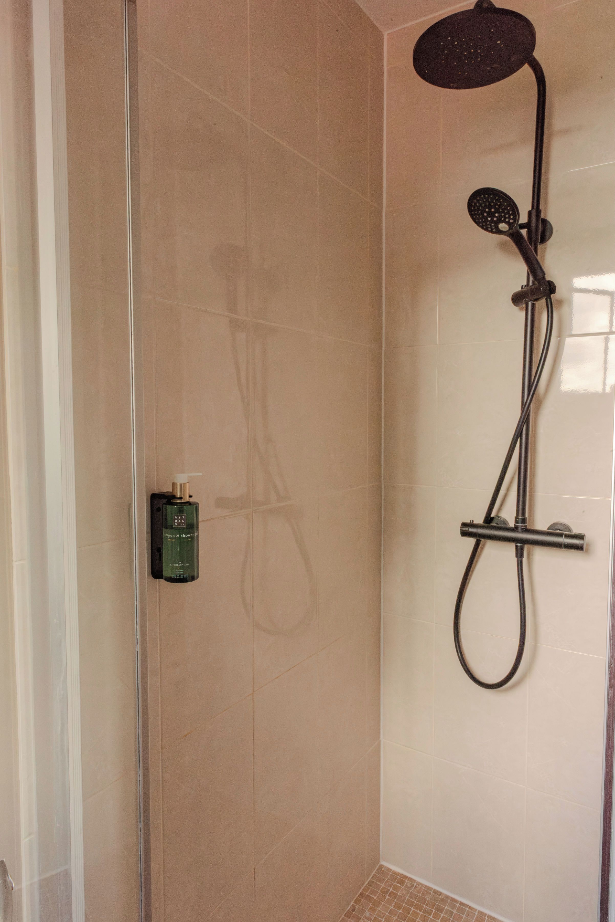 A shower with a handheld showerhead and a handheld scrubber.