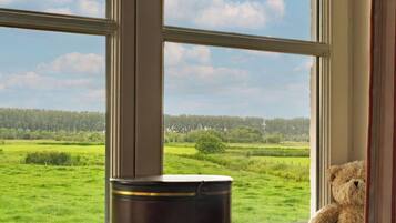 A window with a view of a green field and a teddy bear on the sill.