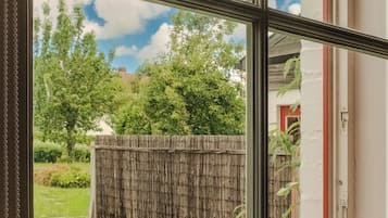 A view through a window of an outdoor seating area with a table and chair, a wooden fence, and greenery.