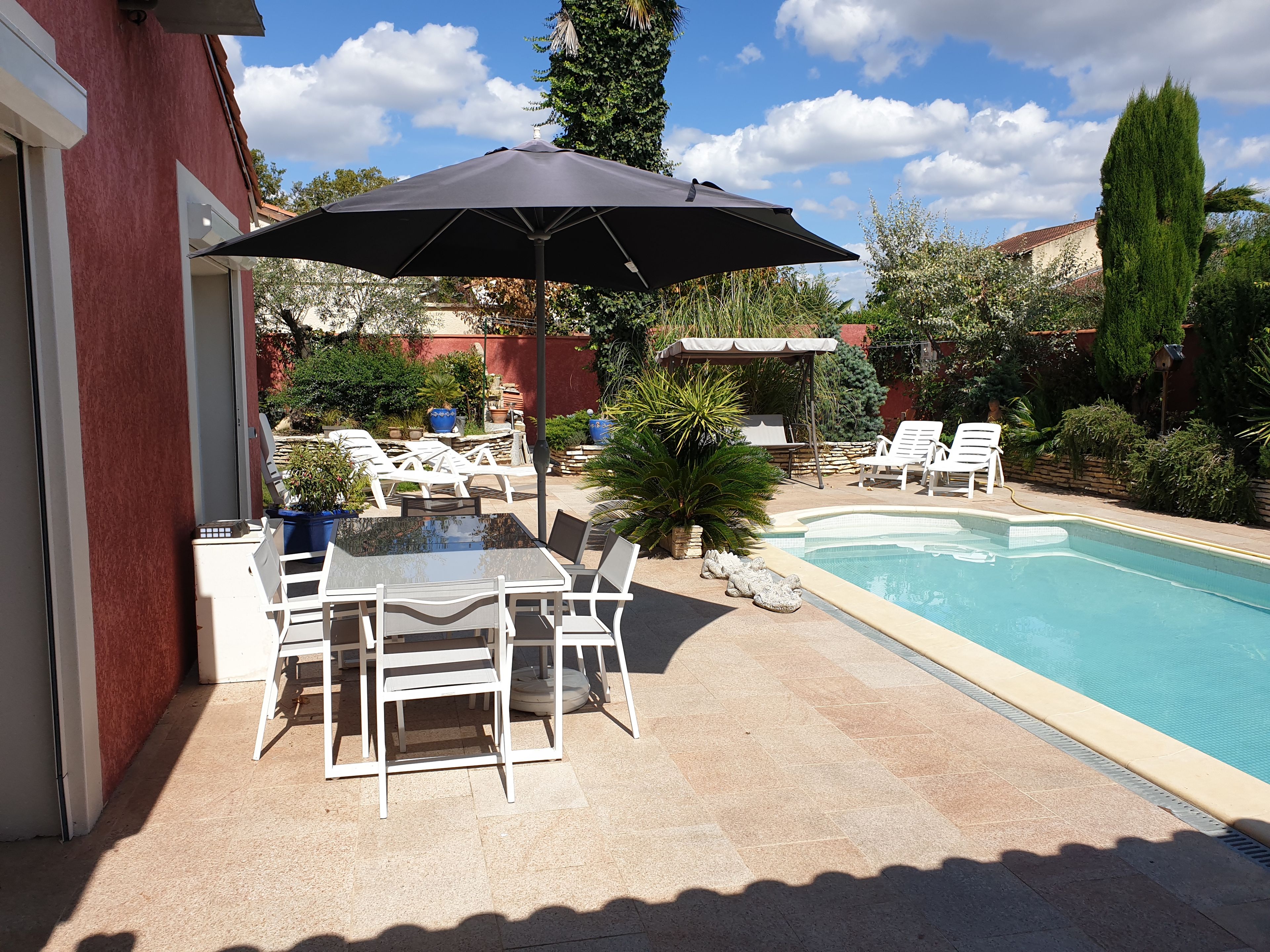 Zona junto a la piscina con mesa y sillas, un espacio de estar techado y una piscina.