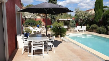 Zona junto a la piscina con mesa y sillas, un espacio de estar techado y una piscina.