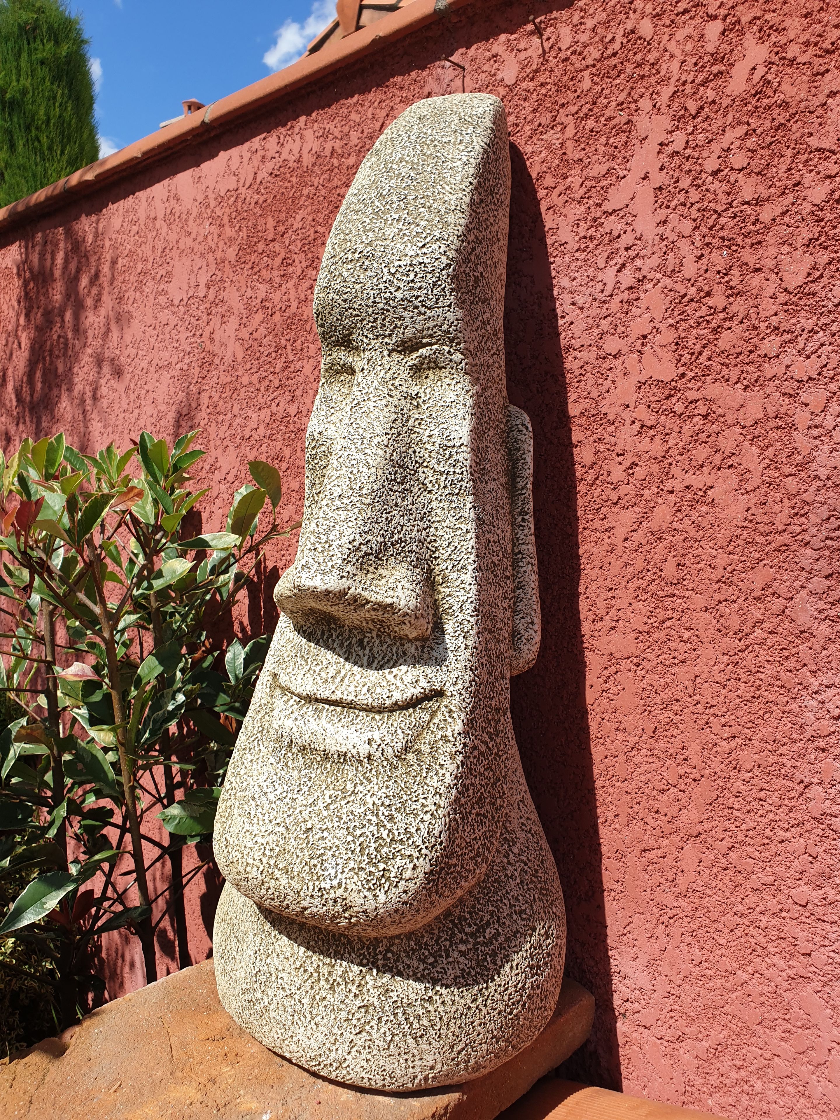 A stone sculpture with a carved face, set against a textured red wall.