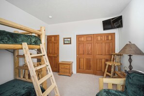 Ein Zimmer mit einem Etagenbett, einer Holzleiter, einem kleinen Holztisch, einer Lampe und einer Tür mit einem Bild an der Wand.