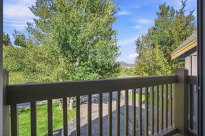 Blick von einem Balkon mit Holzgeländer auf eine grüne Landschaft mit Bäumen und einem entfernten Berg.