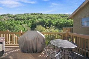 Eine Terrasse mit Grill, Tisch und Stühlen mit Blick auf ein bewaldetes Gebiet.