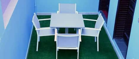 Un pequeño espacio al aire libre con una mesa y sillas, rodeado de paredes azules y césped artificial verde.