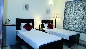 Ein Hotelzimmer mit zwei Einzelbetten, einem kleinen Schreibtisch mit Wasserkocher, Nachttischlampen und einem gemusterten Vorhang.