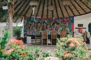 A room with a thatched roof, a colorful mural, wooden chairs, and potted plants. - Quinta Risas del Sol (Brisas de Zicatela)