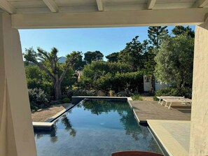Ein Schwimmbecken mit Holzterrasse und Liegestühlen, umgeben von Bäumen und einem Haus.